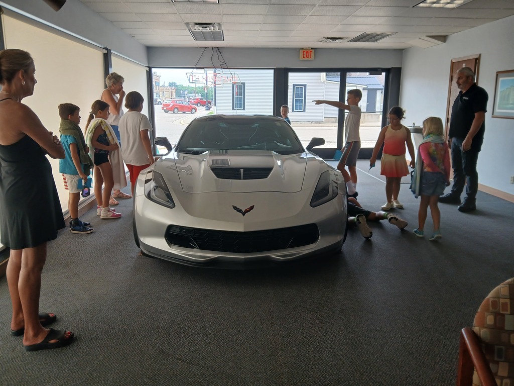 elementary students and teachers with a corvette at a car dealership
