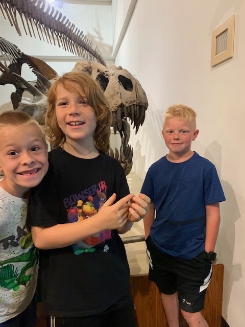 three elementary students with dinosaur skeleton at the University of Wisconsin-Madison' Geology museum