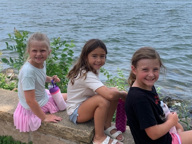 three elementary students by a lake