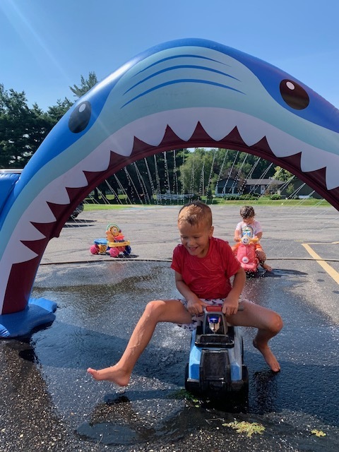 elementary student riding toy bike through shark sprinkler