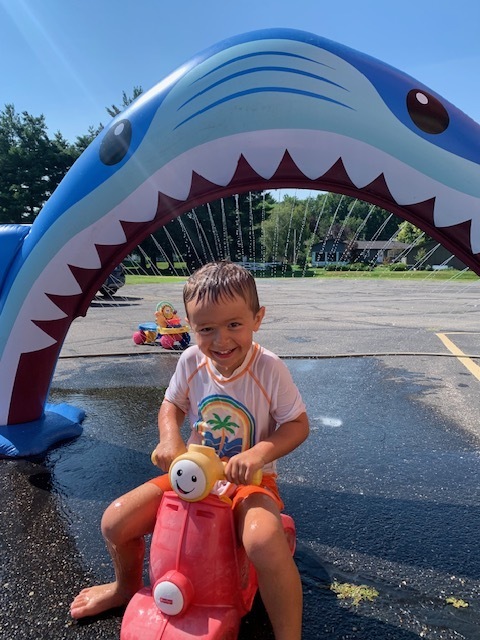 elementary student riding toy bike through shark sprinkler