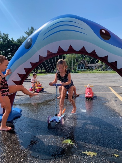 elementary student riding a scooter through shark sprinkler