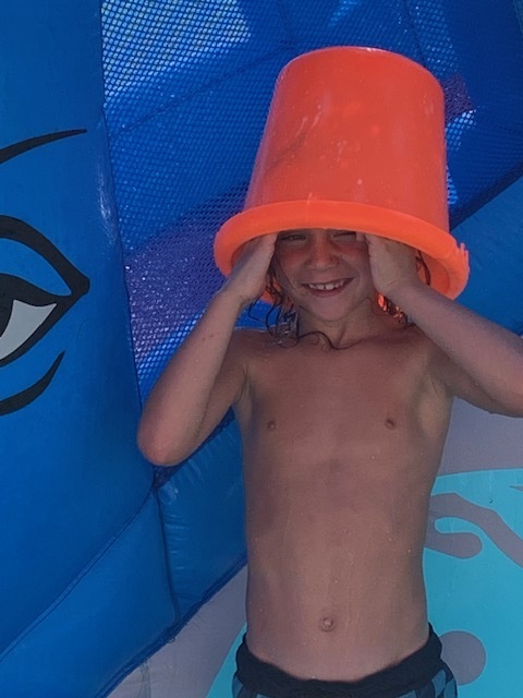 smiling elementary student in blow up pool with bucket on their head