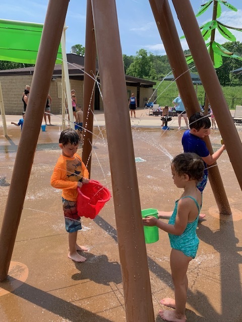 three elementary students playing with buckets at the splash pad