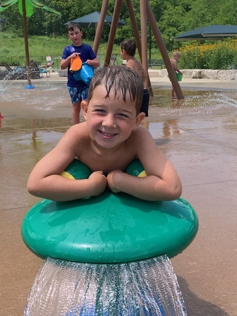 elementary student smiling and leaning on splash pad equipment