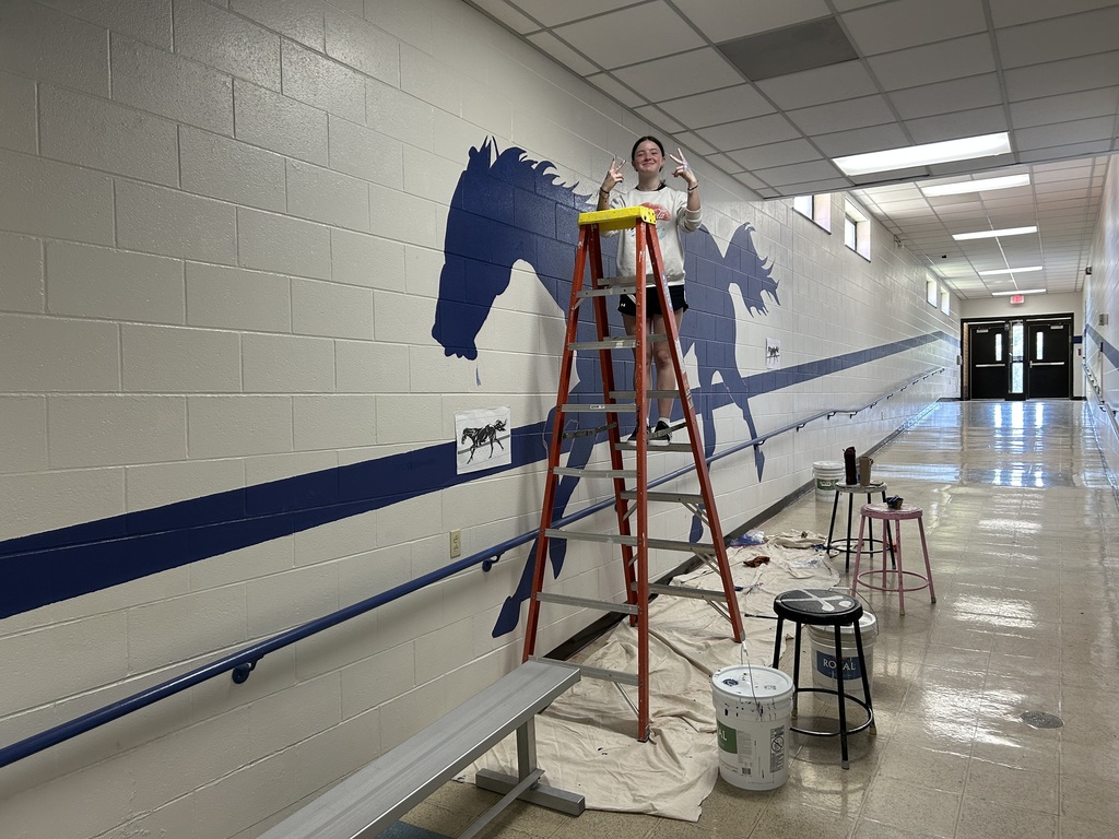 Kalyn Constantini standing beside her mural of Ponies painted along the ramp near the Tech Ed Shop.