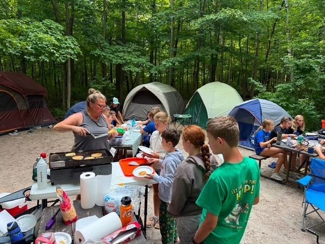 teacher and students getting breakfast at camp by tents