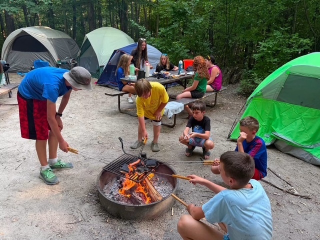 students roasting hot dogs on camp fire by their tents