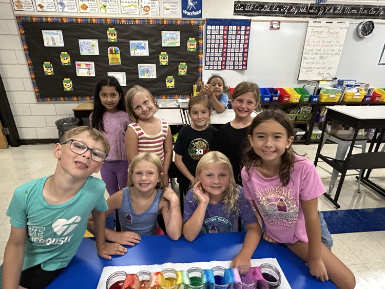 smiling second graders in classroom with rainbow project