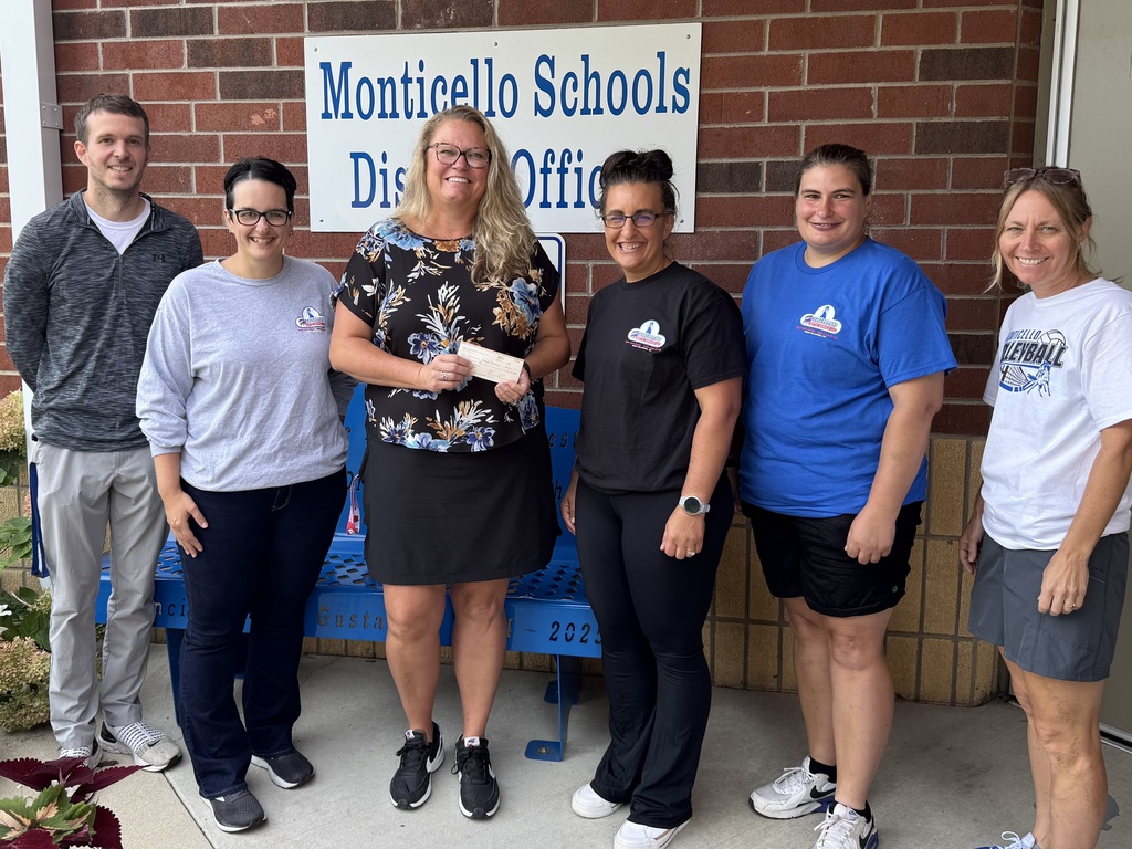 six people standing in front of school with donation check