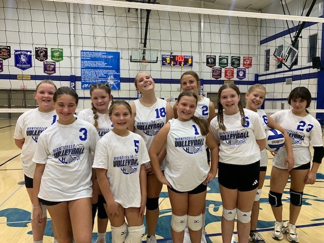 6th Grade Volleyball Players Smiling and Standing In Front of a Volleyball Net