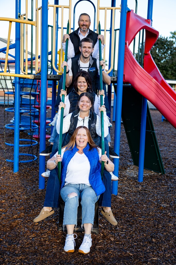 Five staff members sitting on playground stairs.