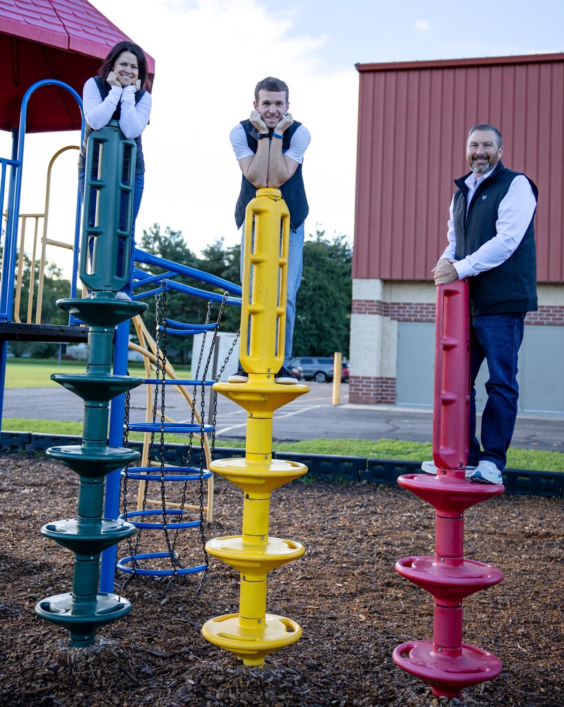 Three staff members standing on playground poles.