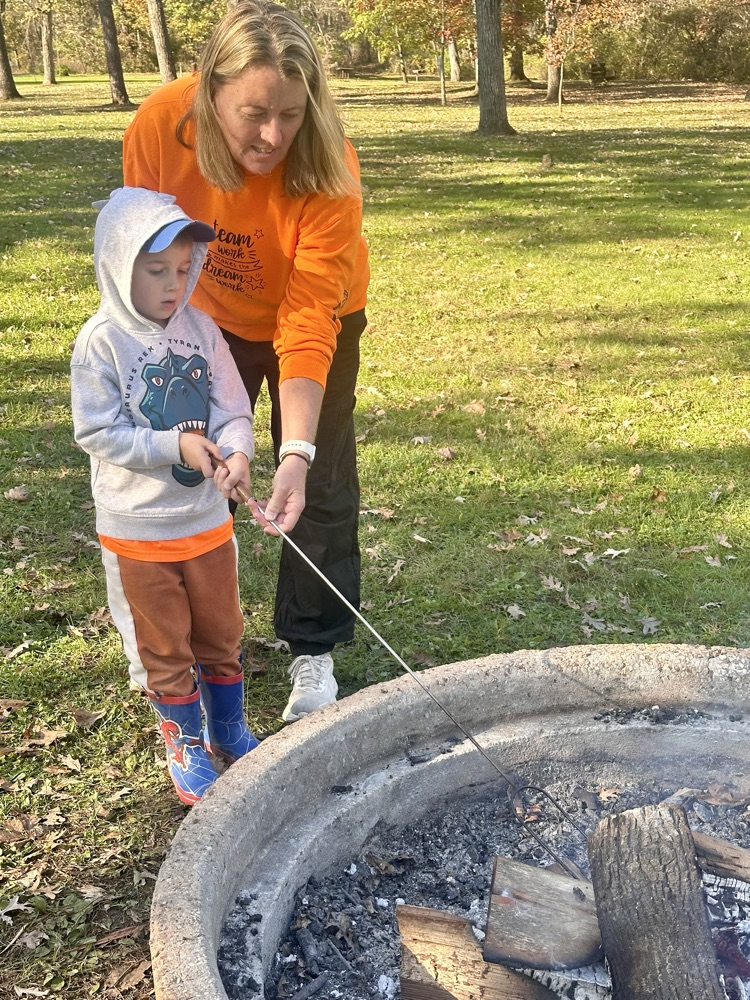 Teacher and student roasting marshmallows at a fire pit.
