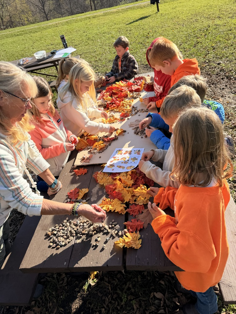 Children and teacher making leaf art on a picnic table.