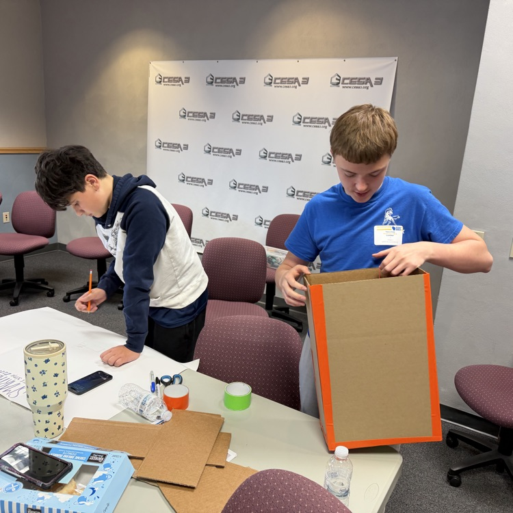 Two FBLA students creating a shaker bed with duct tape and cardboard.
