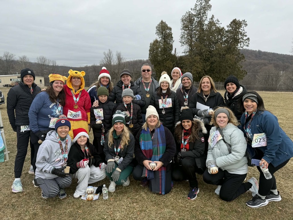 A group of smiling participants, dressed warmly, pose after a fun run. Some wear medals and costumes, conveying a cheerful and festive mood.