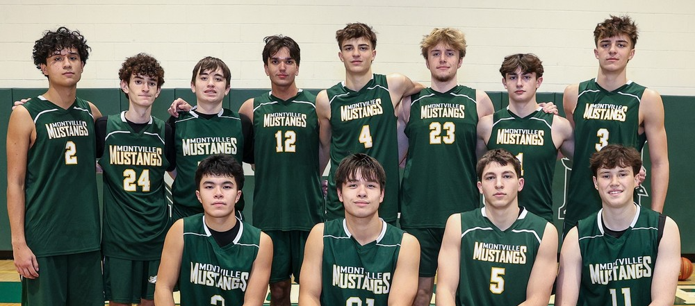 A basketball team in green Montville Mustangs uniforms poses on a court. Eight players stand behind, and five kneel in front, exuding a confident and united spirit.