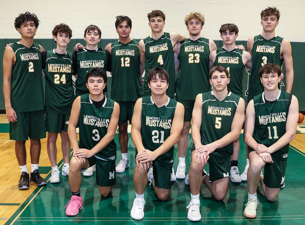 A basketball team in green Montville Mustangs uniforms poses on a court. Eight players stand behind, and five kneel in front, exuding a confident and united spirit.