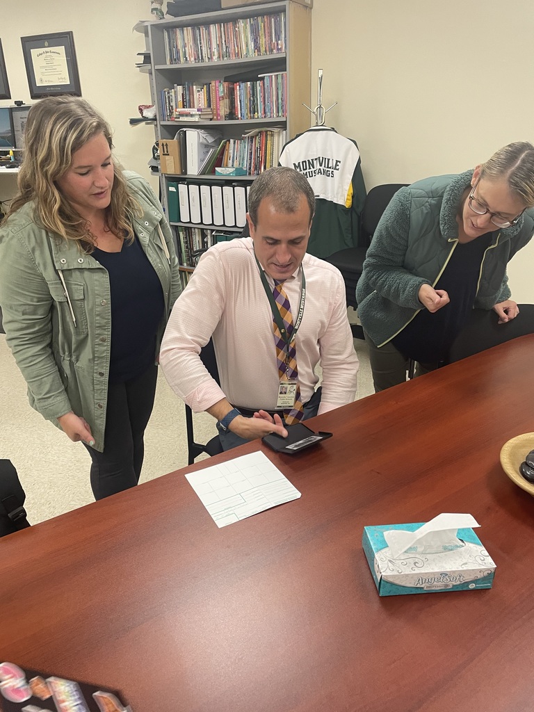 Principal Sanford provides a thumbprint fingerprint using ink . Two teachers stand on either side to help him fill the card correctly.