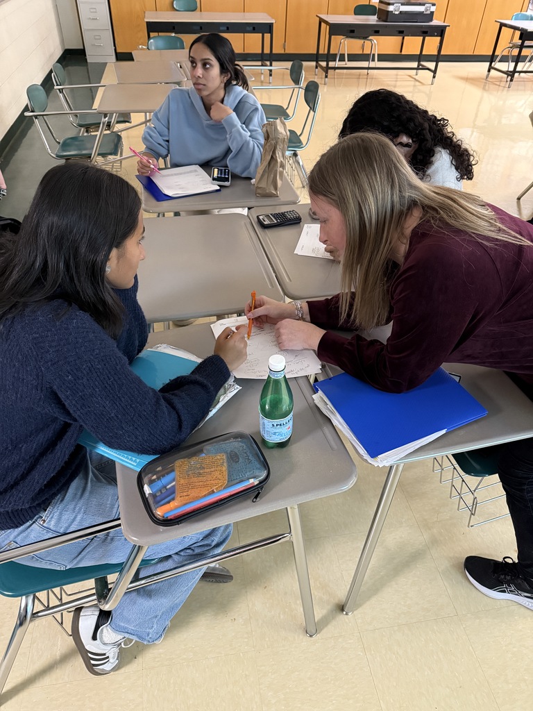 teacher works with a small group of students at desks that are grouped together on a worksheet