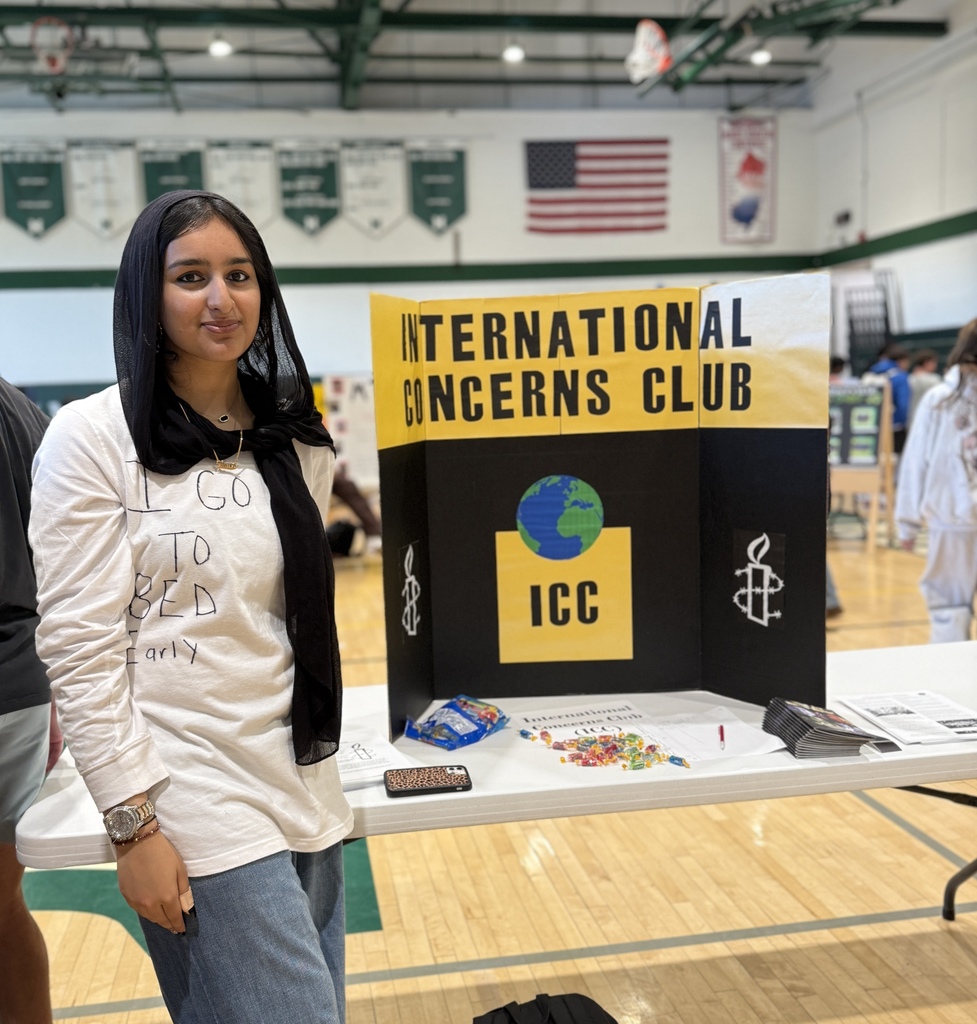 Student stands with International Concerns Club trifold during the annual club fair