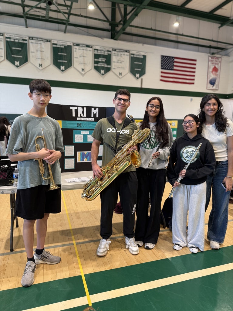 Members of the Tri M club stand with musical instruments and their trifold during the annual club fair