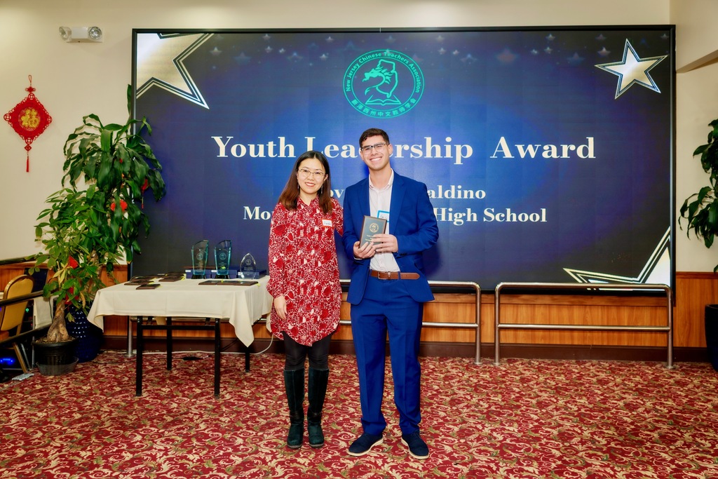 Two people stand proudly in front of a "Youth Leadership Award" display. One holds a plaque. The setting is formal, with a celebratory atmosphere.