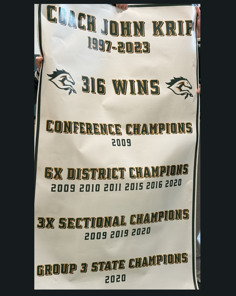 Close up of the new banner honoring Coach John Krip that says: Coach John Krip 1997-2023/ 316 wins/ 2009 Conference Champions / 6X District Champions (2009, 2010, 2011, 2015, 2016, 2020) / 3x Sectional Champions (2009, 2019, 2020) and Group 3 State Champions 2020