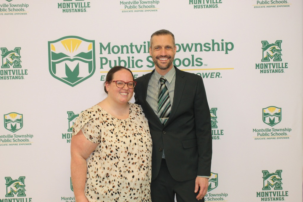 Two people smile in front of a Montville Township Public Schools backdrop. They appear confident and happy, dressed in professional attire.