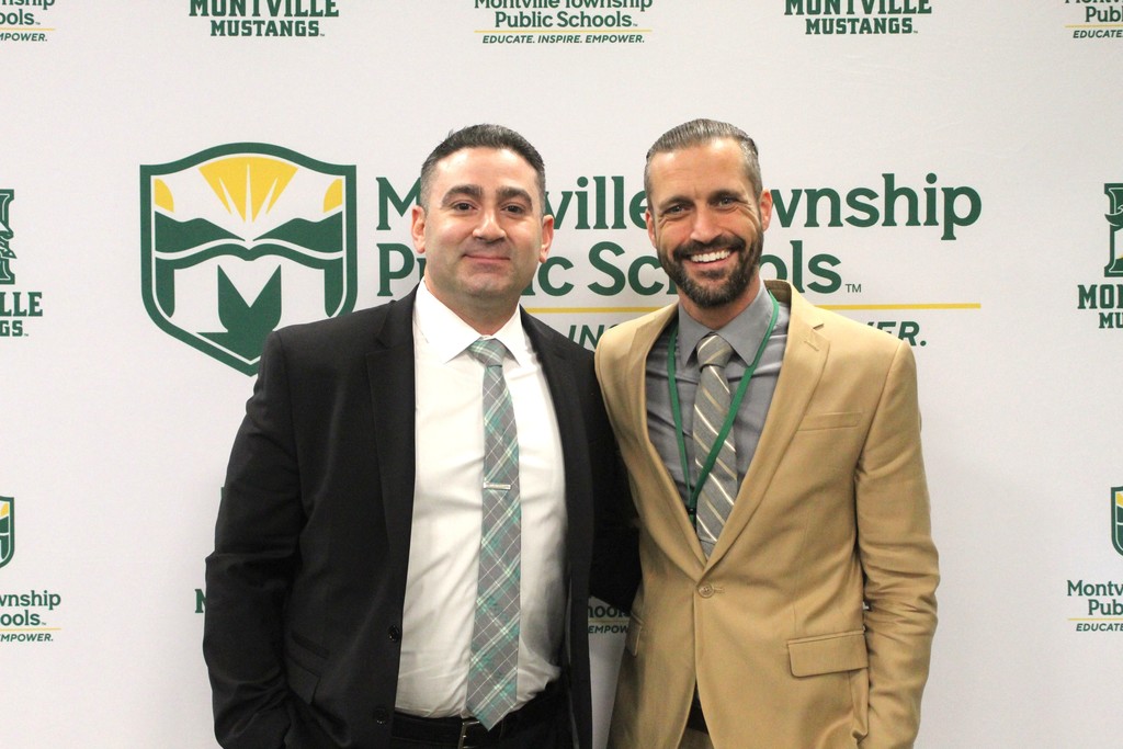 Two men in suits smiling in front of a Montville Township Public Schools backdrop. The mood is professional and friendly, conveying positivity.