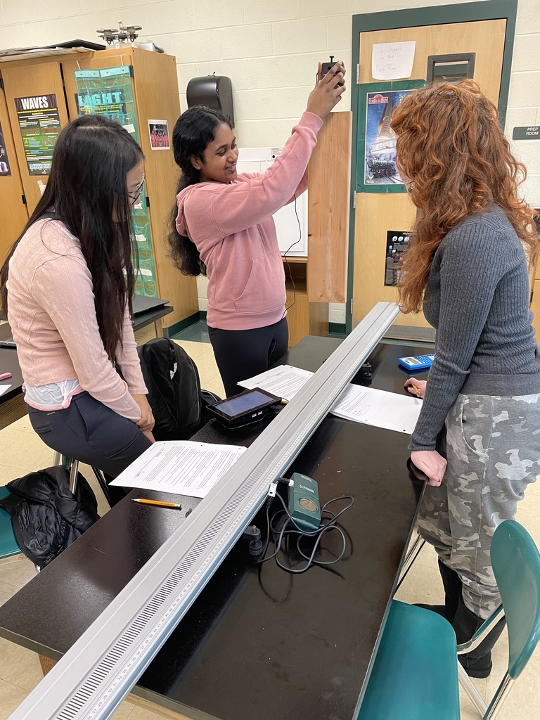three students work to weigh the block of wood used in a lab to analyze static and kinetic friction