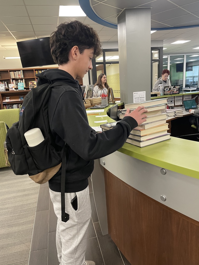 Student adding a book to a large pile of book returns.