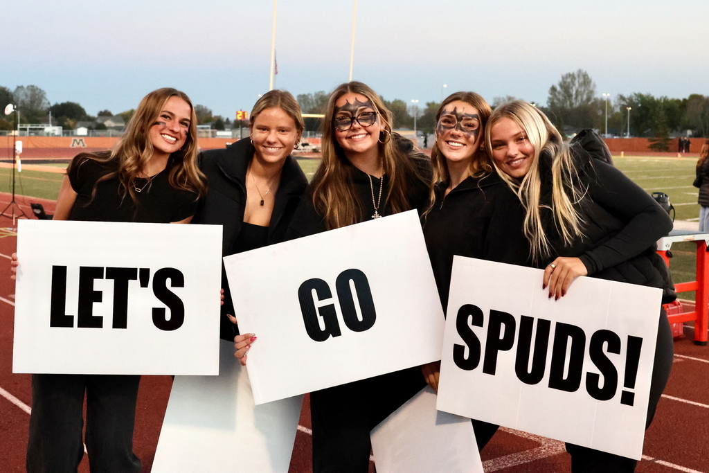 5 senior girls hold up signs to help lead spud fans in sweet caroline chant at moorhead high school football game