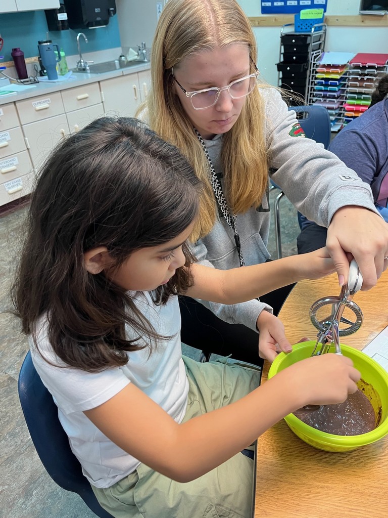Student mixing chocolate pudding with a staff member helping.