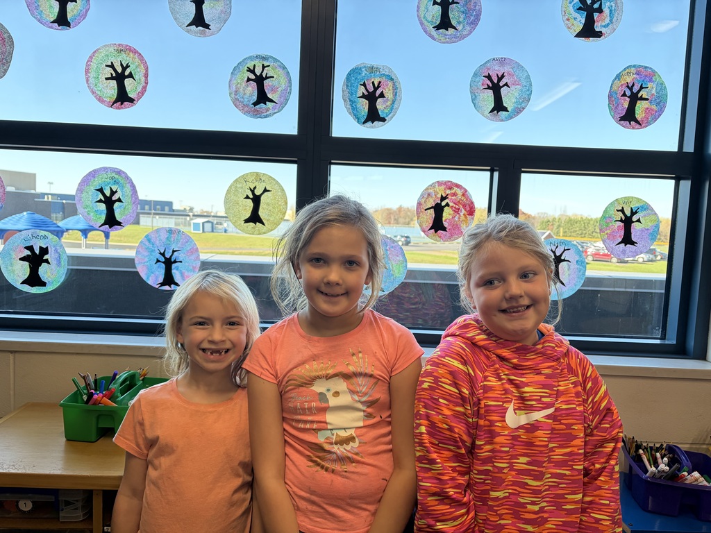 Visual Description: A bright indoor photograph of elementary-aged students standing side-by-side in a classroom, smiling shoulder to shoulder..