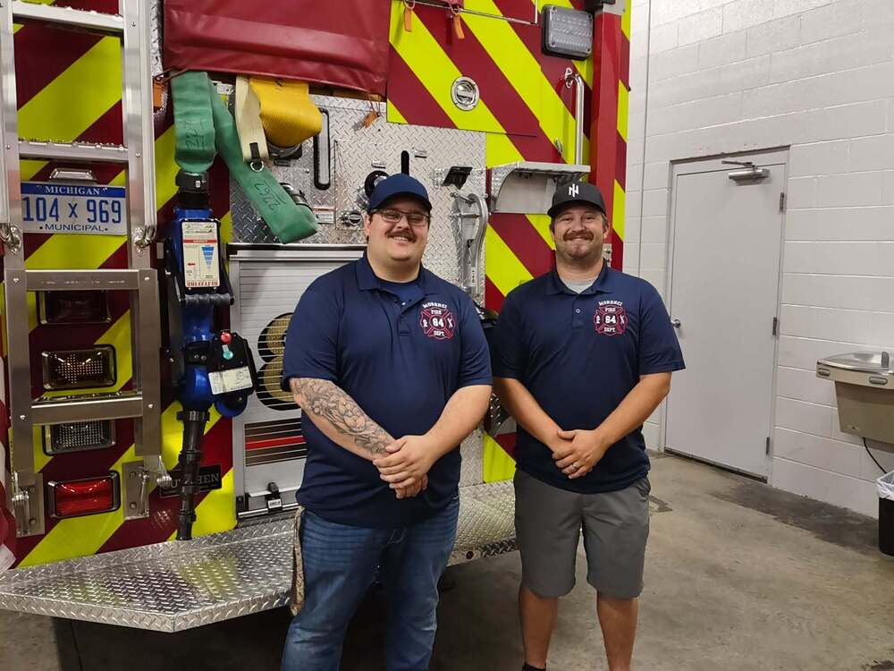timothy schisler and colin richardson standing behind fire truck smiling