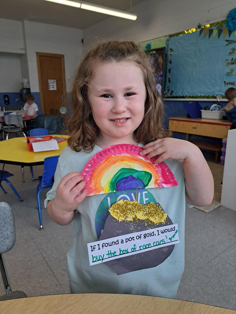 student holding a painting of a rainbow and pot of gold.