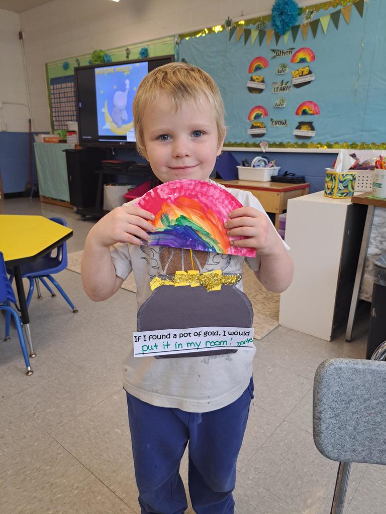student holding a painting of a rainbow and pot of gold.