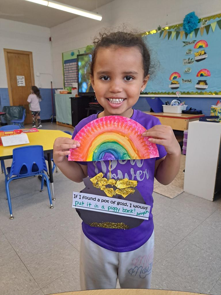 student holding a painting of a rainbow and pot of gold.