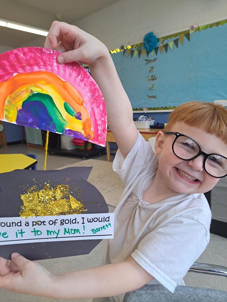student holding a painting of a rainbow and pot of gold.
