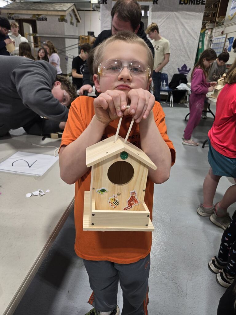 student showing off his birdhouse he made.
