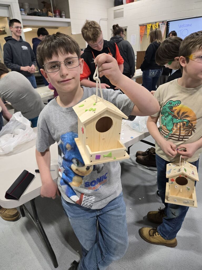 student showing off his birdhouse he made.