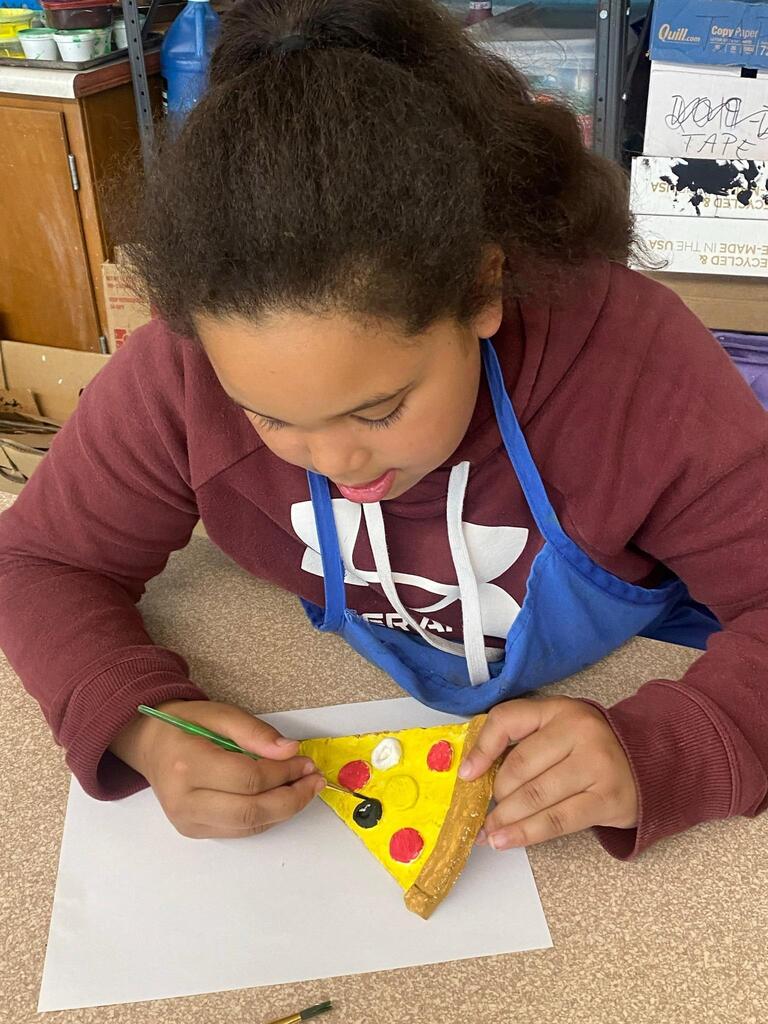 student creating ceramic slice of pizza and coloring it.