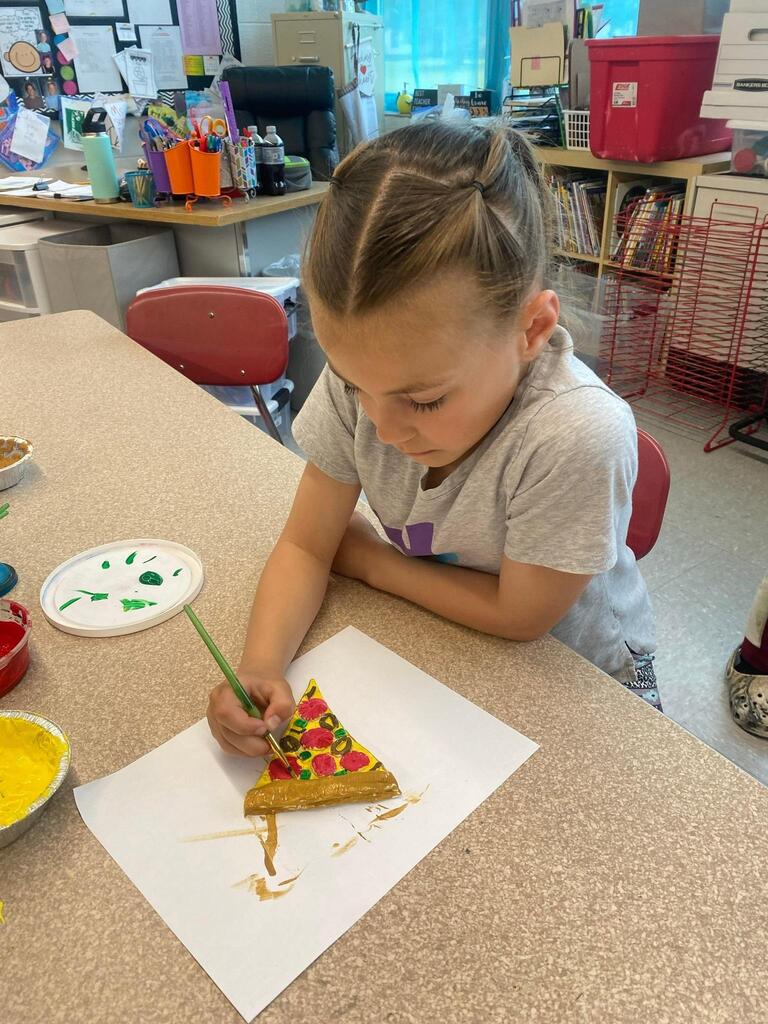 student creating ceramic slice of pizza and coloring it.