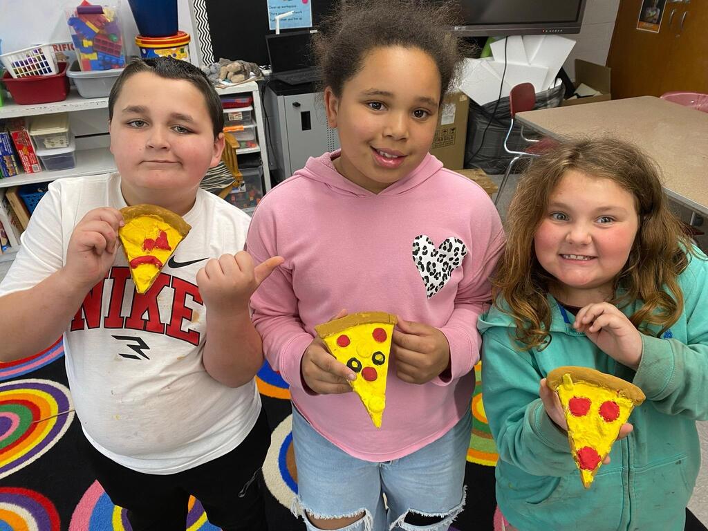group of students showing off their final piece of pizza all painted.
