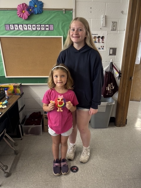 Kindergarten and 8th grade student posing for picture with the stuffed animal that was made for them.