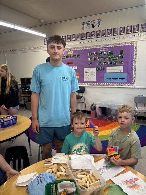 Kindergarten and 8th grade student posing for picture with the stuffed animal that was made for them.