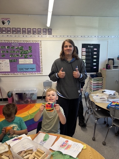 Kindergarten and 8th grade student posing for picture with the stuffed animal that was made for them.
