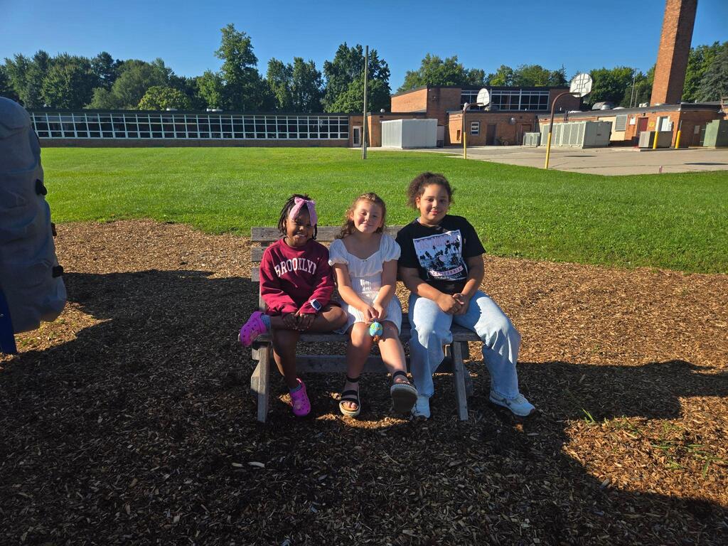 three students sitting outside on the bench